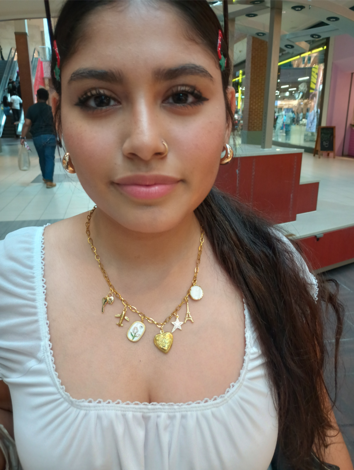 Woman wearing a gold charms necklace with heart and star pendants in a mall setting